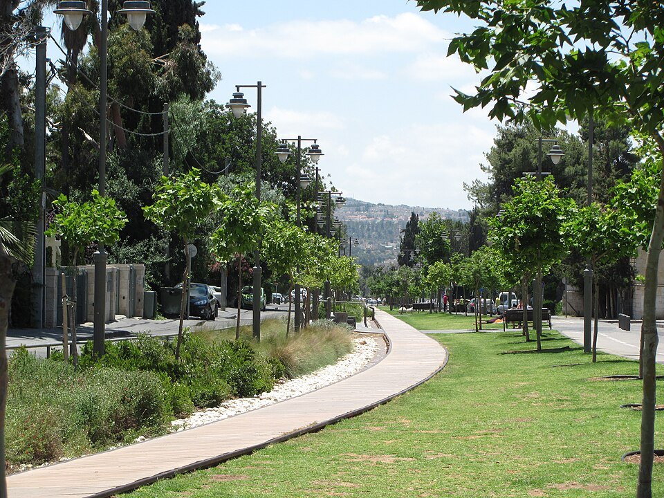 השביל המרוצף המתפתל בפארק המסילה בירושלים, לצד רצועות דשא ועצים צעירים