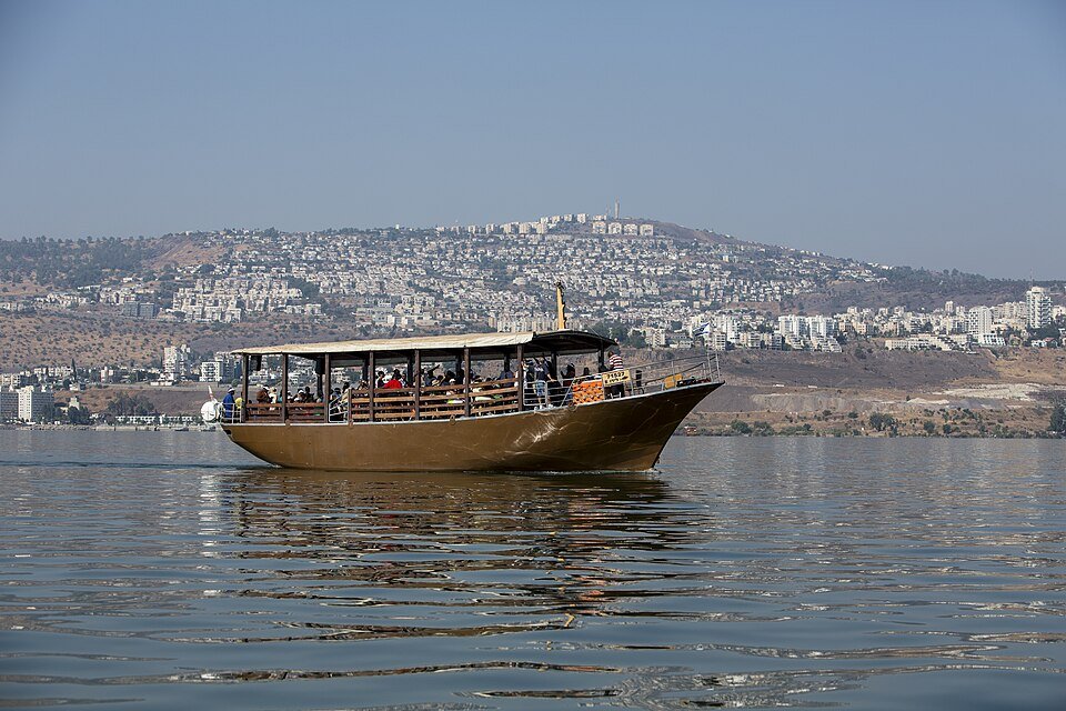 ספינת עץ שטה על פני הכנרת, עם גבעות הגליל ברקע